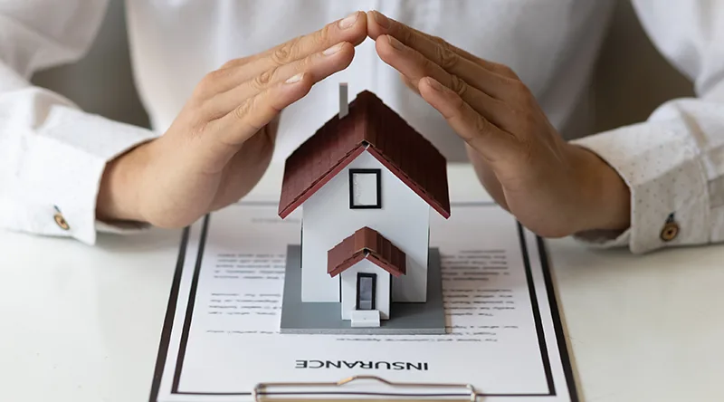 Hands sheltering a home, homeowners insurance protection