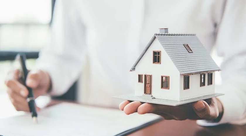 Homeowner signing an insurance policy while holding a model house